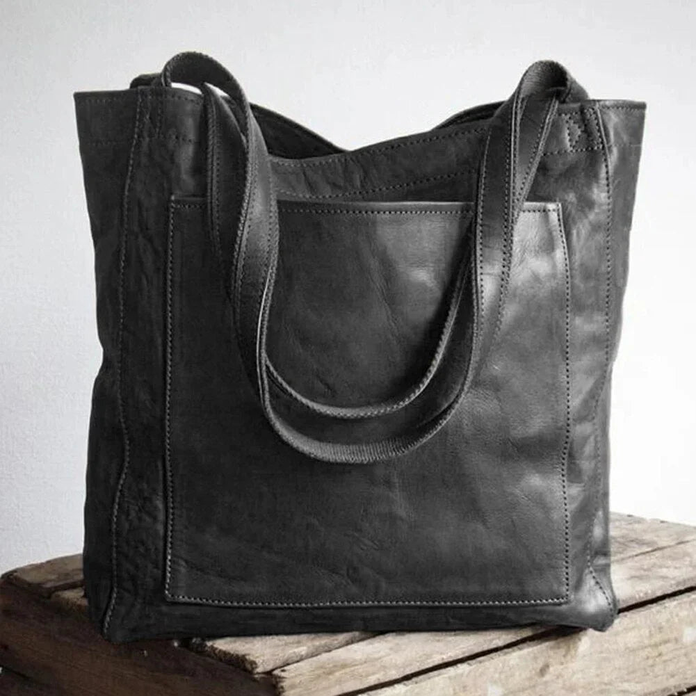 Black leather tote bag with magnetic snap closure and front patch pocket.