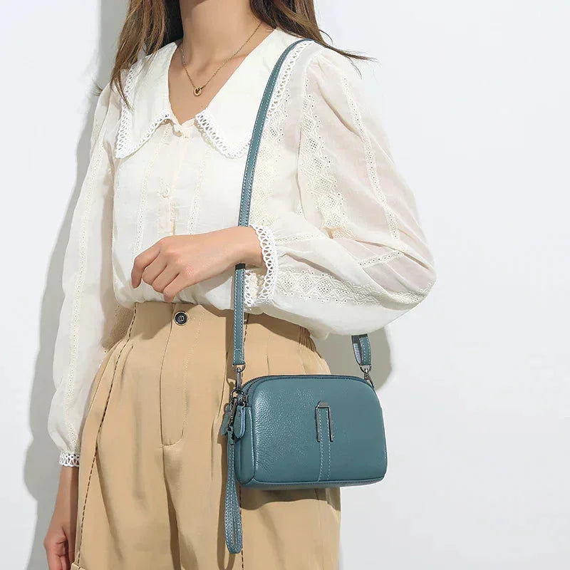 Blue leather shoulder bag with double zip closure and metal accent.