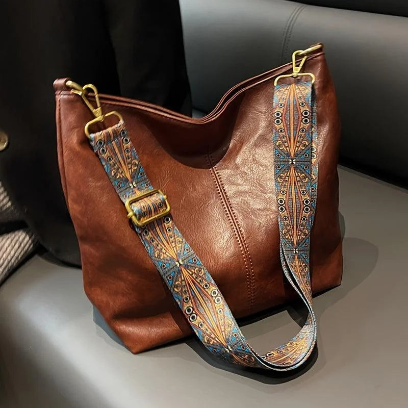 Brown faux-leather hobo bag, wide bohemian-patterned strap.