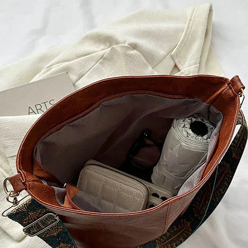 Brown faux-leather hobo bag with a wide, bohemian-patterned strap.