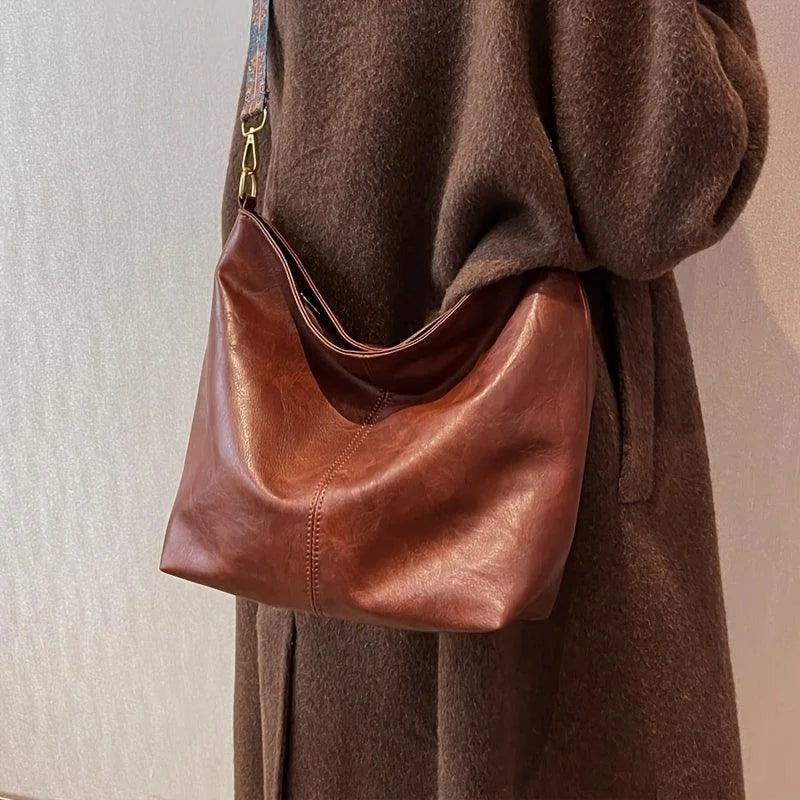 Brown faux-leather hobo bag with a wide, bohemian-patterned strap.